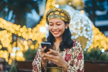 A cheerful woman in traditional clothing using her smartphone during a festive moment, showing how easily the WA777 app fits into everyday life.