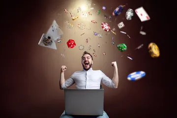 A man celebrating a winning moment on his laptop while gaming symbols float around him, capturing the excitement of WA777 games.