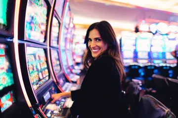 A woman smiling by bright slot machines showing lucky symbols, showcasing the exciting slot offerings at WA777.